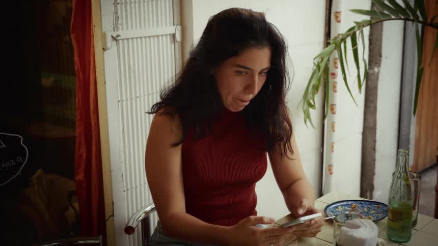 A woman sits at an outdoor cafe table while focused on her smartphone as the camera slowly pushes in