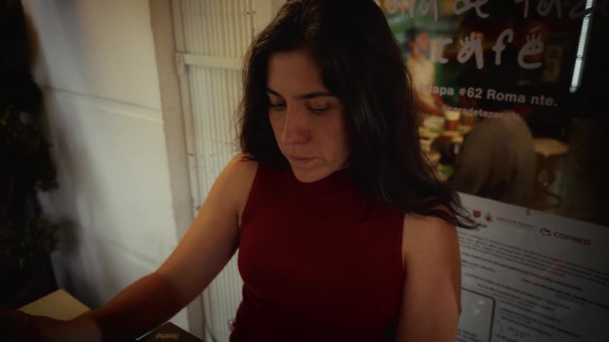 A woman in a cafe opens her laptop and is struck with shock and despair by what she sees on the screen