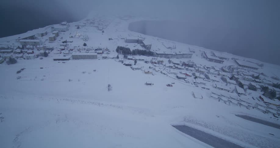 A dramatic aerial view flying over a snow-covered coastal village shrouded in thick fog