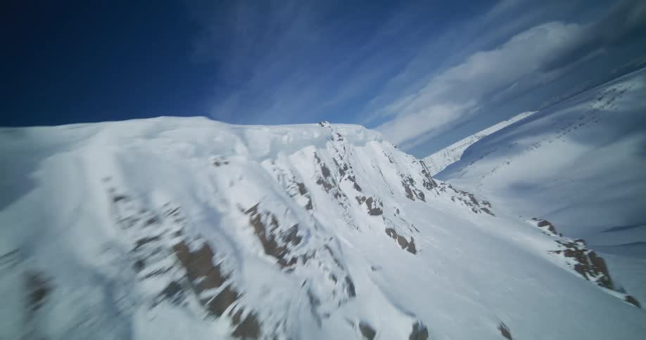An exhilarating aerial flight ascending a steep, snow-covered mountain face under a vast blue sky
