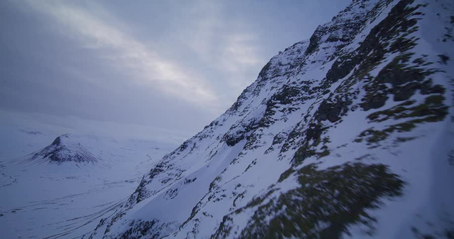 A majestic aerial tracking shot along a steep, snow-covered mountain in a vast, frozen landscape