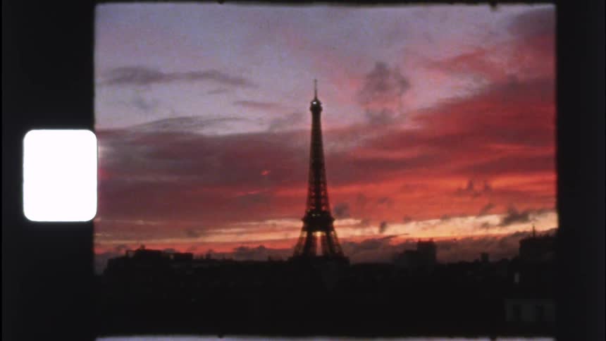 Vintage 8mm footage shows the Eiffel Tower silhouetted against a dramatic and colorful sunset over Paris, France