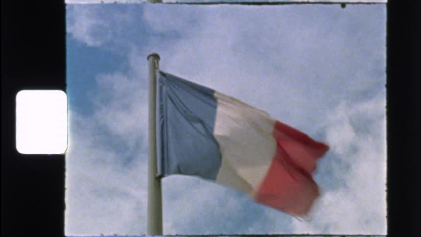 A grainy, vintage 8mm shot captures the French flag waving in the wind against a cloudy sky