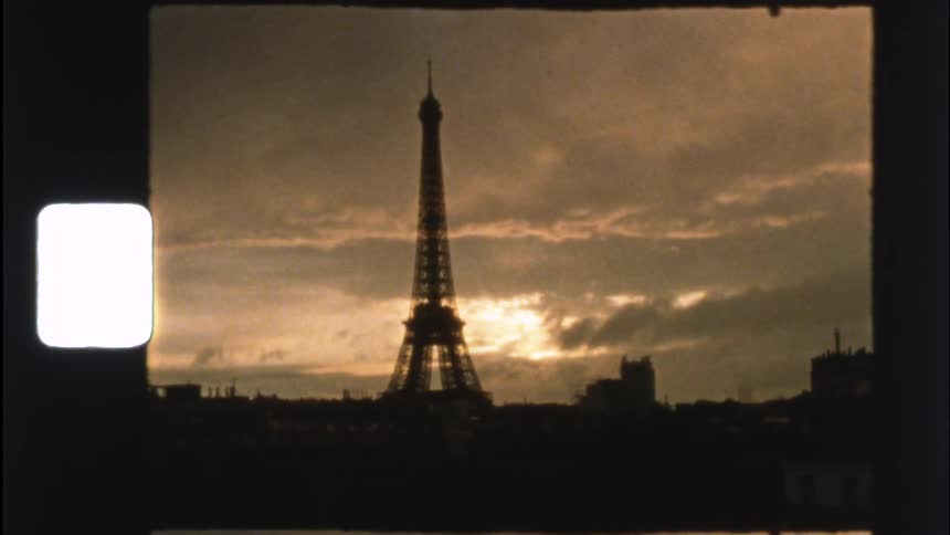 A vintage 8mm film captures the silhouette of the Eiffel Tower in Paris against a dramatic sunset sky
