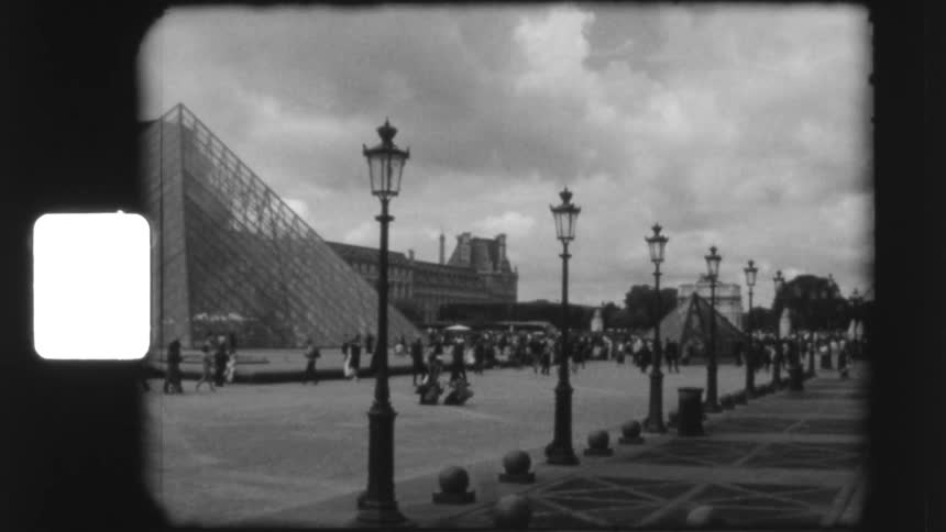 A vintage super 8mm black and white panning shot captures tourists walking through the courtyard of the Louvre Museum and its iconic glass pyramid in Paris