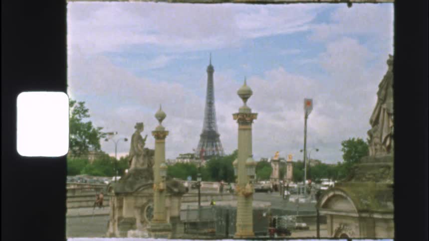 Vintage 8mm film shows the iconic Eiffel Tower in Paris, framed by ornate statues and columns on a historic bridge