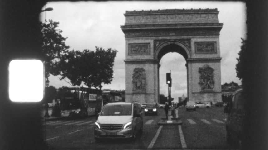 A grainy, black and white vintage super 8mm film captures the bustling traffic around the iconic Arc de Triomphe in Paris