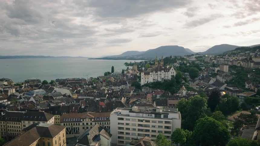 A scenic wide shot of the historic city of Neuchâtel, Switzerland, nestled on the shore of a vast lake with mountains in the distance