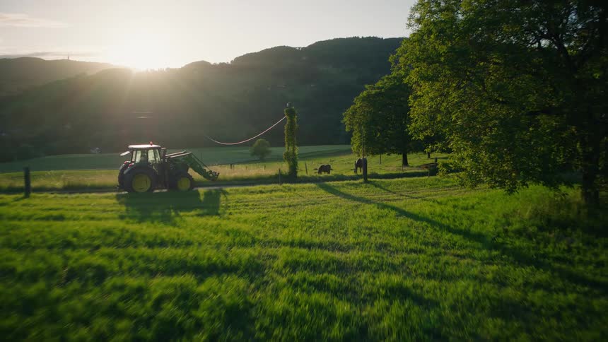 Aerial shot of a tractor transporting a traditional Maypole through a scenic countryside landscape during a beautiful golden hour sunset