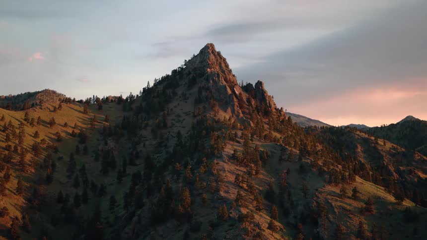 A slow aerial pullback reveals a vast mountain range with a prominent peak catching the last light of sunset