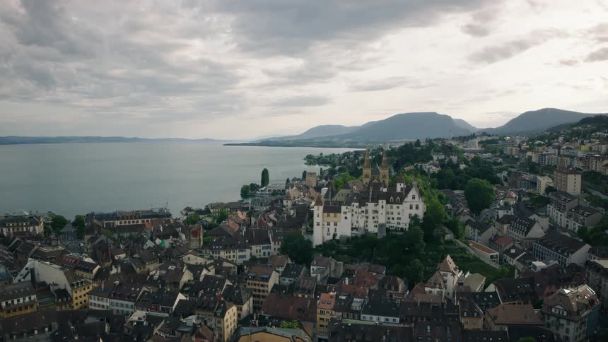 A stunning panoramic view of a historic European city and its grand castle on the edge of a large lake under a cloudy sky