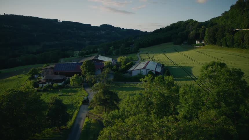 An idyllic farm with solar panels on the roof is nestled in the rolling green hills as a tractor drives up the country lane at sunset