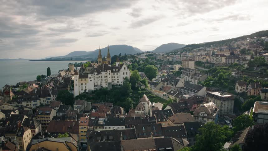 Expansive aerial pull-back shot revealing the historic city of Neuchâtel, Switzerland, with its iconic castle overlooking the vast lake and distant mountains