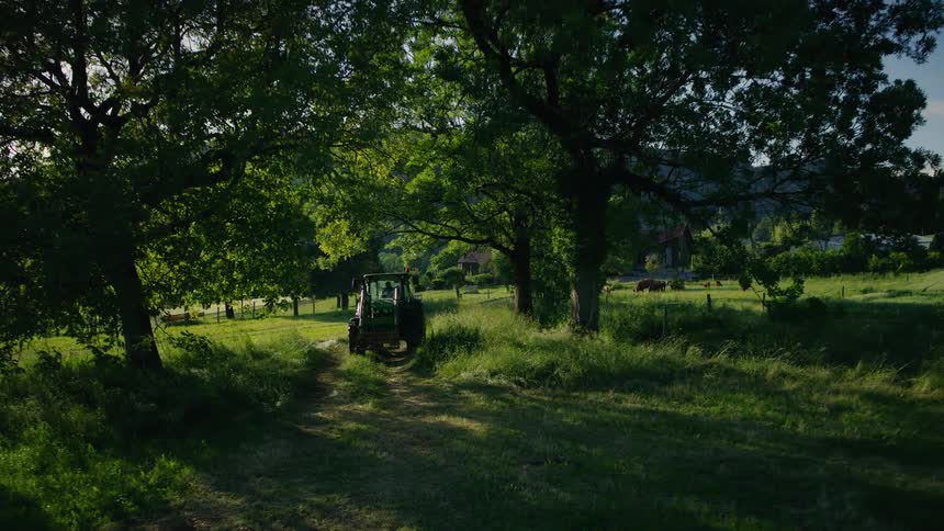A slow pull-back shot reveals a green tractor parked on a tranquil country lane amidst a lush, rolling green landscape during a beautiful sunset