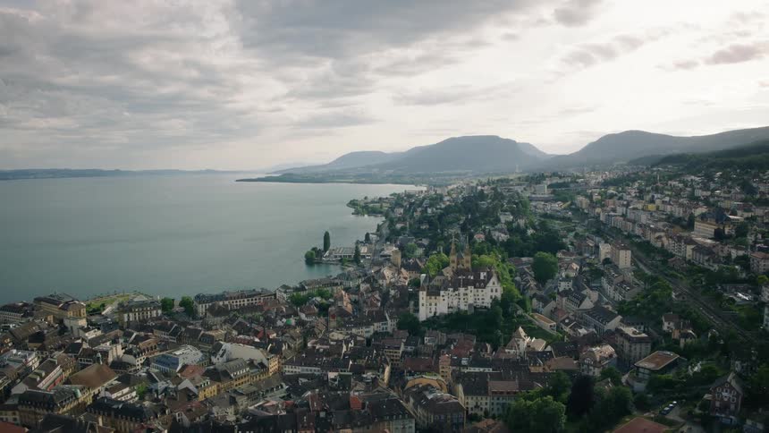 A scenic aerial view reveals the historic city of Neuchâtel, Switzerland, nestled on the shores of a vast lake with mountains in the background