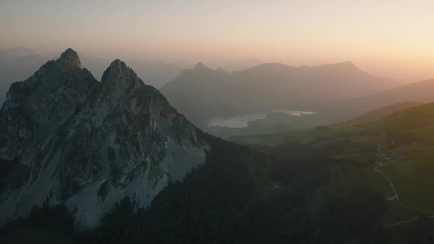 Stunning aerial view of the majestic Grosser Mythen mountain peaks overlooking a lush valley and distant lake during a hazy sunrise