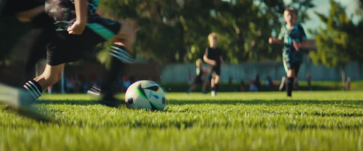 A low-angle view of a youth soccer game, focusing on players dribbling and kicking the ball across the grassy field