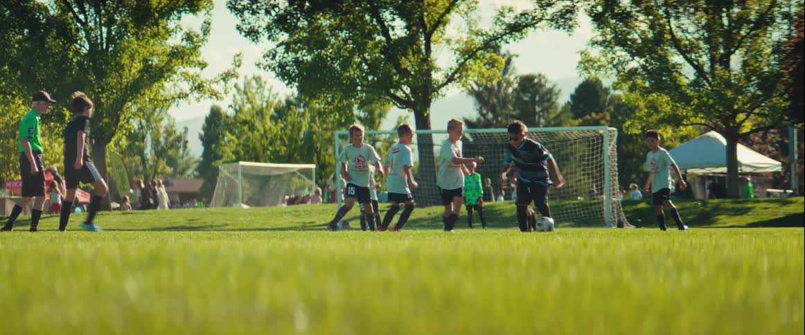 low angle shot pulls focus from the green grass to kids playing soccer on a sunny day