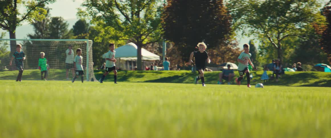 A group of young boys run across a vibrant green field chasing a soccer ball during a game on a sunny day