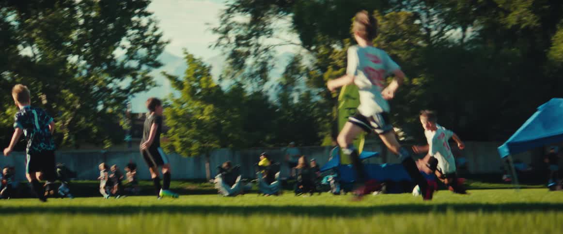 A side-view tracking shot captures the energy of young boys running down a green field during a competitive soccer game