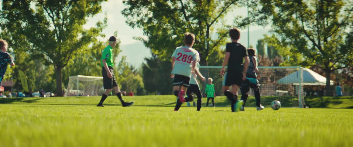 Young boys chase after a soccer ball during a competitive game on a sunny day