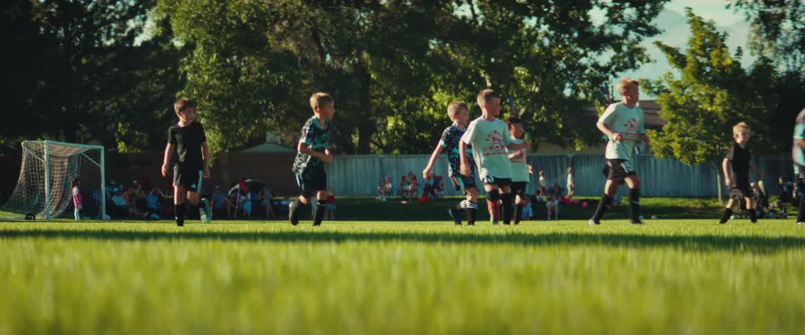 A group of young boys run down a grass field during a competitive soccer game on a sunny day