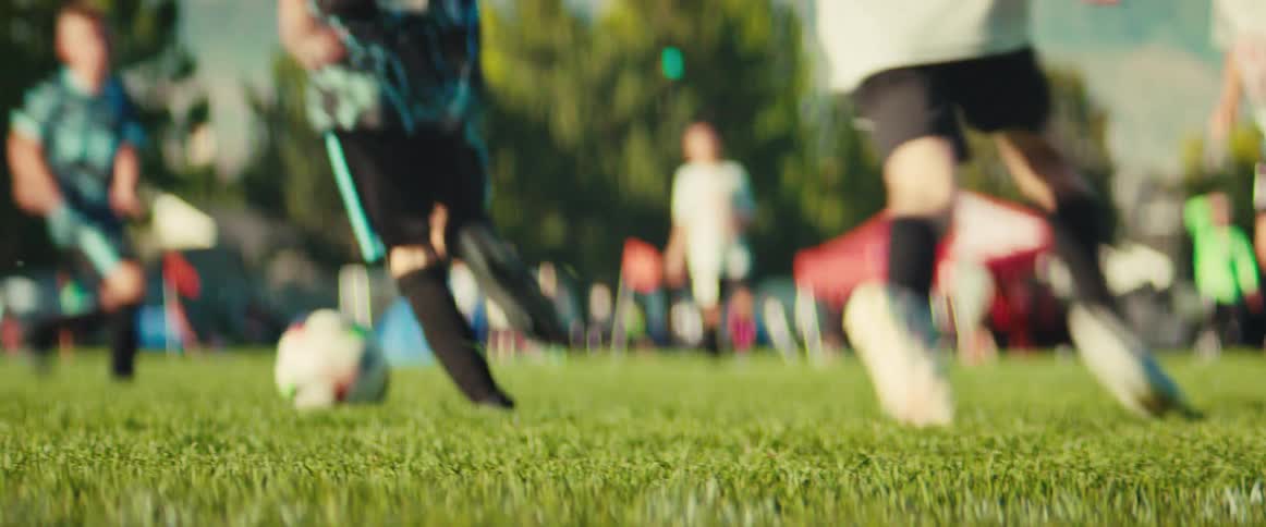 A dramatic low-angle shot captures the intense action as young boys chase and kick a soccer ball during a competitive game