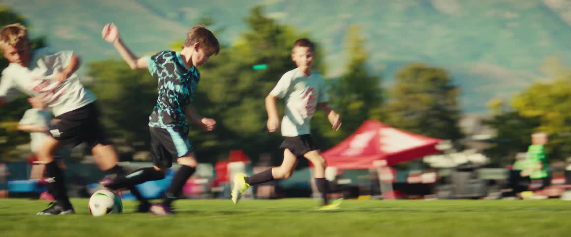 Energetic young boys compete for the ball during a soccer game on a grassy field with mountains in the background