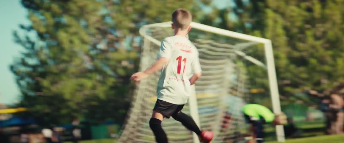 A young boy dribbles a soccer ball down the field past defenders in a competitive match