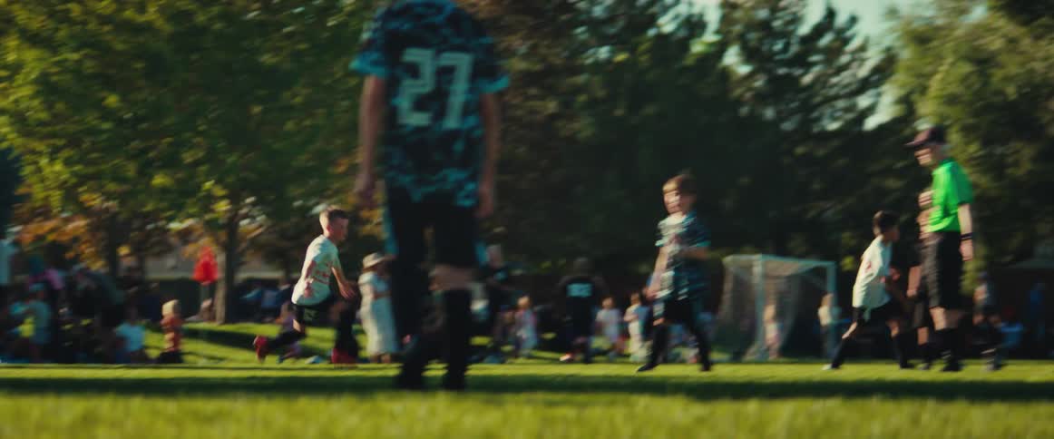 In slow motion, a young boy is tackled and a goal scored during a competitive youth soccer game as parents watch from the sidelines