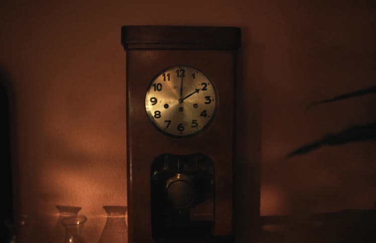 A vintage wooden pendulum clock ticks quietly on a wall in a dimly lit room at night
