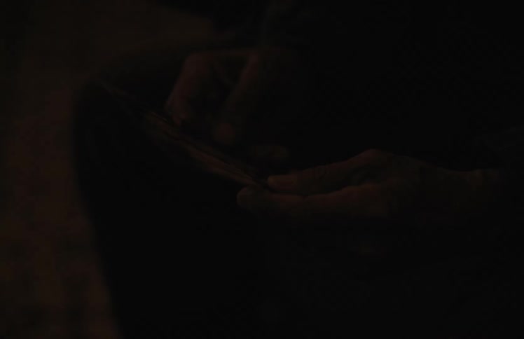 A close-up shot of an elderly person's weathered hands holding a cherished old photograph in a dark, dimly lit room