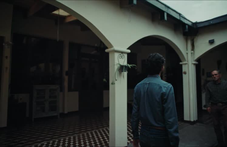A young man and an older man reunite and share a warm, heartfelt embrace in the open courtyard of a traditional home
