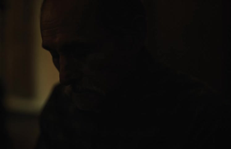 An intimate slow focus shot reveals the contemplative face of an older man with a mustache in a dimly lit room