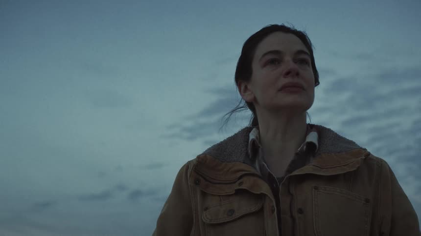 A woman stands outdoors under a cloudy sky at dusk, breathing deeply as she finds a moment of peace and hope