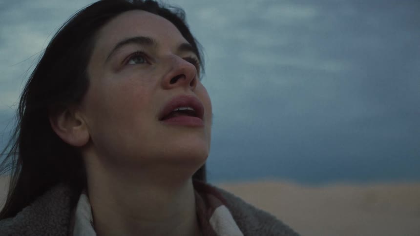 An emotional close-up of a contemplative woman breathing deeply as the wind blows through her hair against a dusky sky