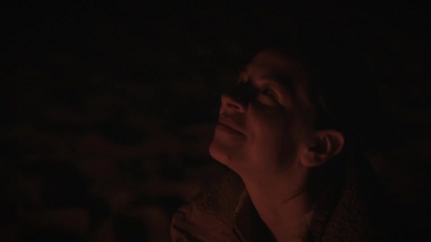A woman smiles peacefully as she is illuminated by the warm glow of a campfire at night