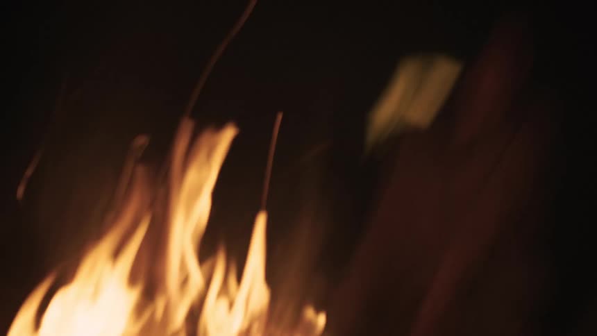 A smiling woman warms her hands over a crackling campfire on a dark night at her campsite