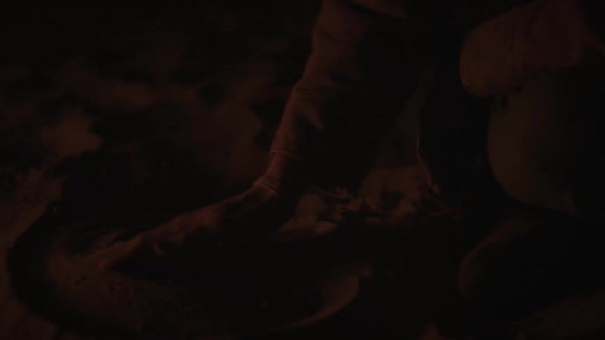 A person's hands draw mysterious circles in the sand by the glow of a bonfire at night