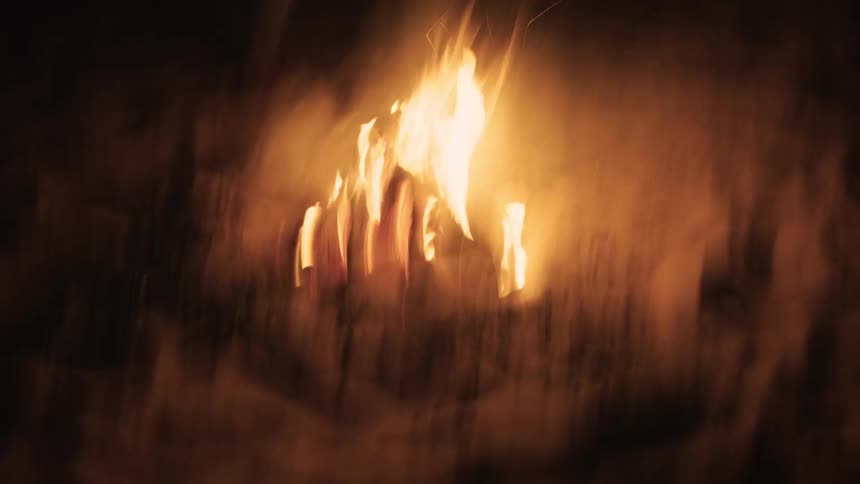 Disorienting handheld footage captures a figure moving around a crackling bonfire in the snow at night