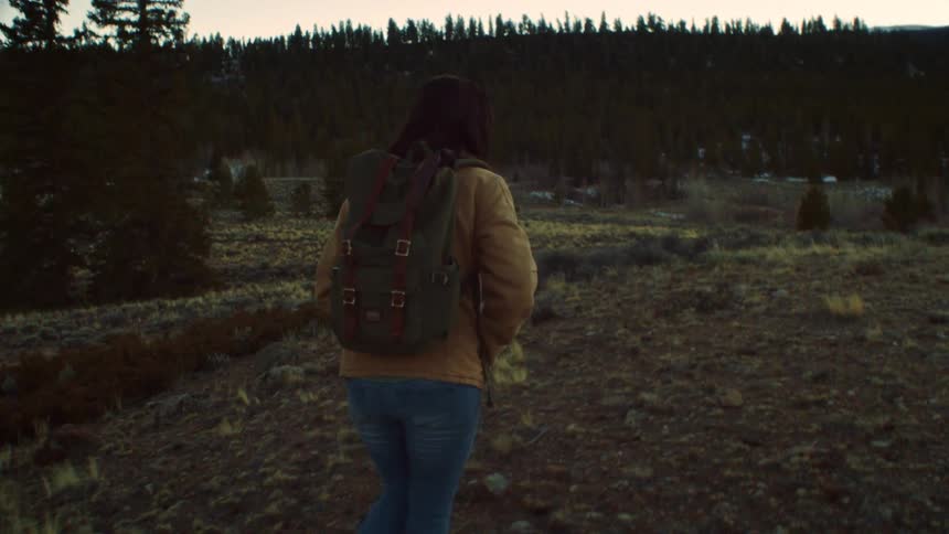 Following a solitary female hiker as she explores a mountain trail at dusk in slow motion