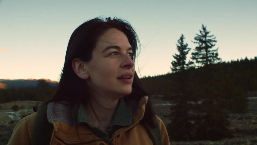 A female hiker's smile turns to awe as she gazes at the beautiful, quiet wilderness during golden hour