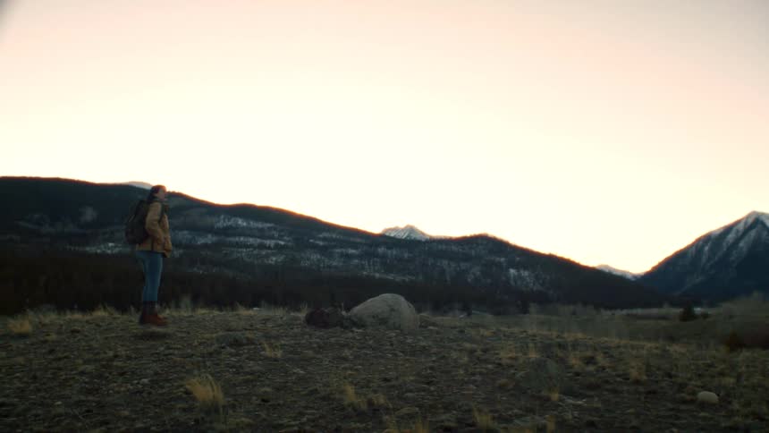 A solo hiker with a backpack walks to a scenic mountain overlook to admire the view at sunset