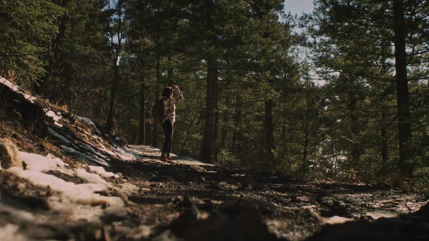 A woman hiker stops on a snowy, sunlit forest trail to admire the distant view