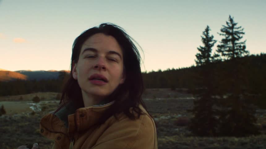 A weary woman with a backpack takes a deep breath while looking out at the beautiful forest landscape during sunset