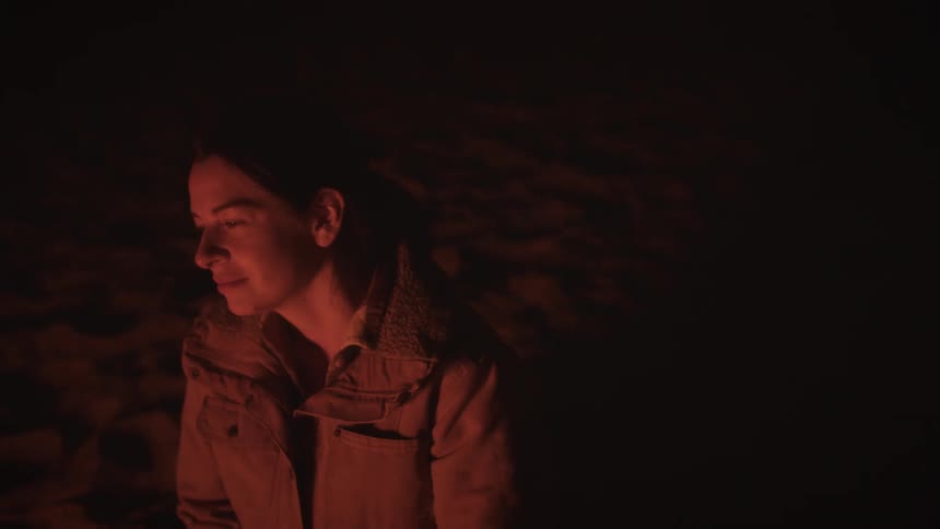 Close-up of a woman's peaceful face illuminated by the red glow of a fire in the dark