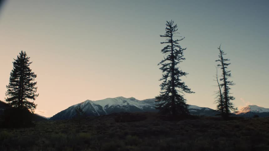 A solitary figure stands silhouetted against a vast, snow-capped mountain range at dawn