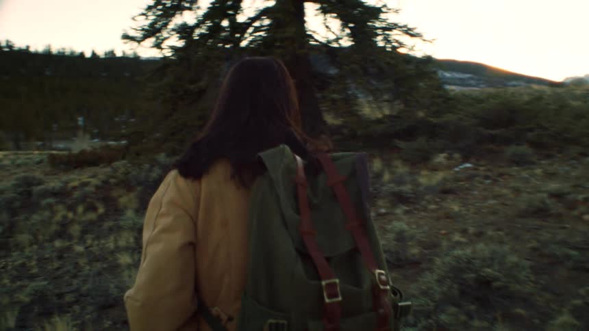 Following a woman with a green backpack as she hikes through a high desert landscape towards snow-capped mountains in slow motion