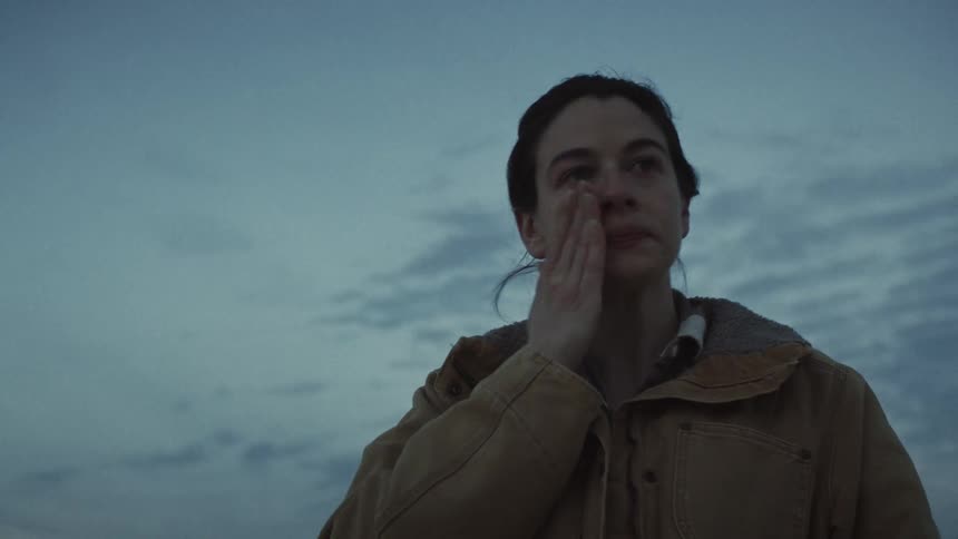 Low-angle shot of a distressed woman in a heavy jacket crying as she looks up at the overcast sky