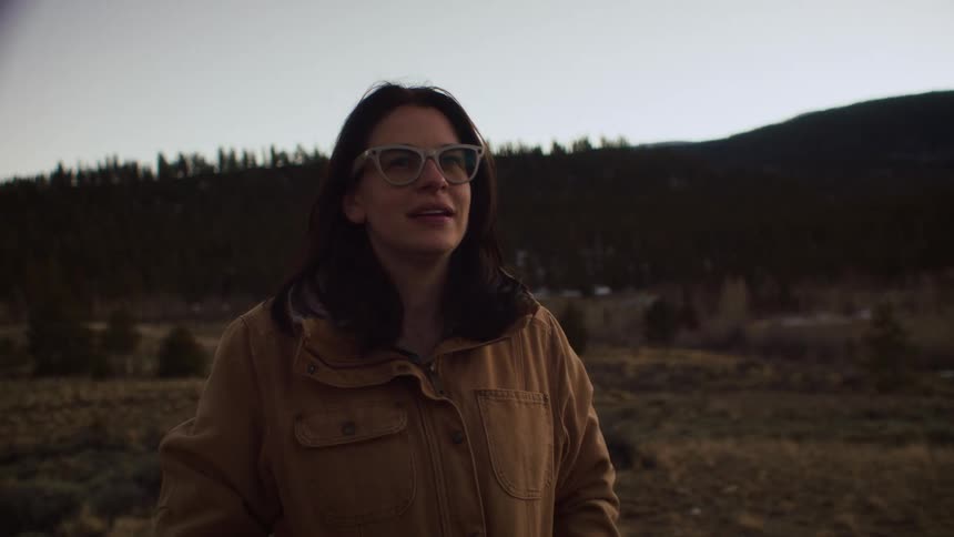 A young woman puts on glasses and enjoys the fresh air in a tranquil, natural landscape at dusk